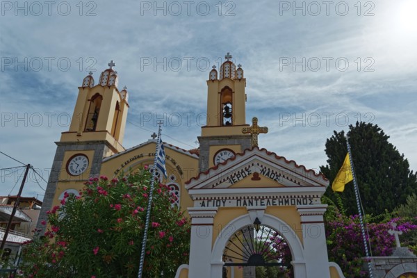 Yellow church with decorative entrance gate and bell towers against the sky, Greek Orthodox Church of Saint Pantaleon, Siana, Rhodes Island, Greece