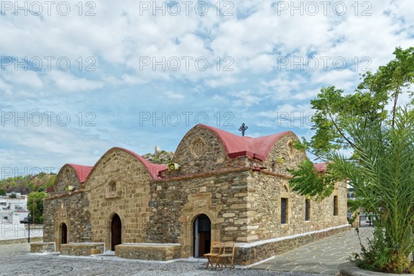 Small stone church Kimisis tis Theotokou with red roofs, surrounded by trees under a clear blue sky, Greek Orthodox Church Kimisis tis Theotokou, Asklipiio, Rhodes Island, Greece