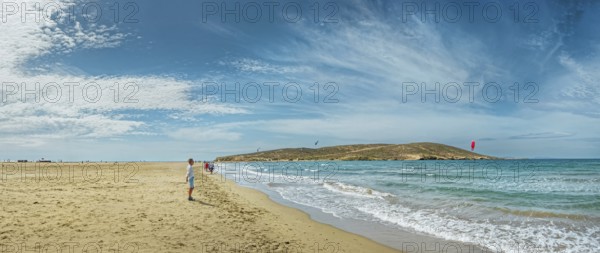 Wide sandy beach of Prasonisi with gentle waves, distant peninsula and kite surfers under a blue sky, Prasonisi, Rhodes Island, Greece