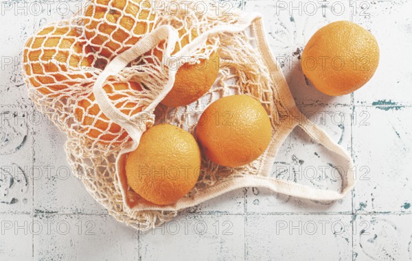 Oranges in a mesh bag, on a textured surface, sunlight, no people