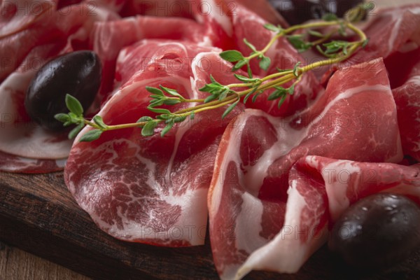 Freshly cut dried meat, served with olives and herbs, on a wooden chopping board, no people
