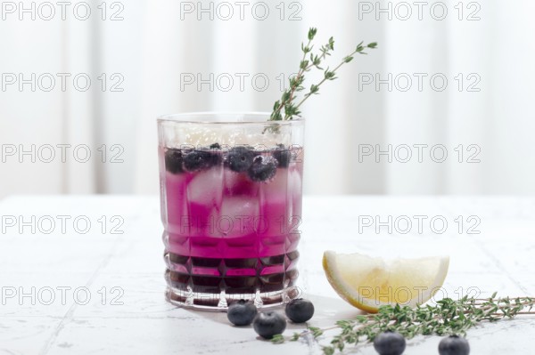 Refreshing blueberry and thyme drink served with lemon in a clear glass on a light surface