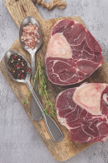 Freshly sliced beef legs, two ossobuco steaks, on a wooden board, with spices and herbs, ready to cook