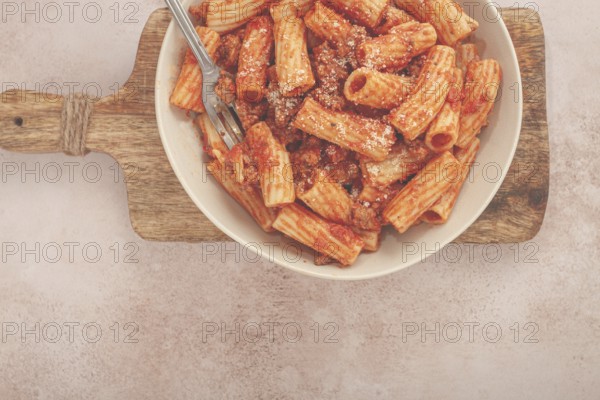 Rigatoni pasta with meat sauce and parmesan cheese on a light table, top view, homemade, no people