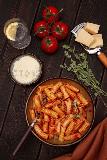 Rigatoni pasta with meat sauce and parmesan cheese on a dark wood table with ingredients, top view