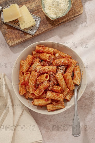 Rigatoni pasta with meat sauce and parmesan cheese on a light table, top view, homemade, no people