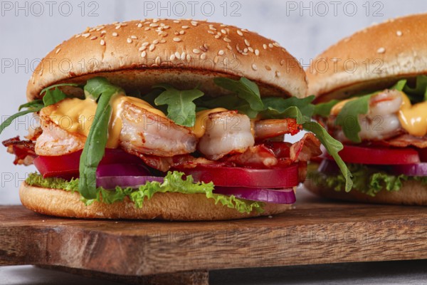 Two shrimp burgers and buns with sesame seeds, bacon, lettuce, tomatoes and onions, On a wooden board