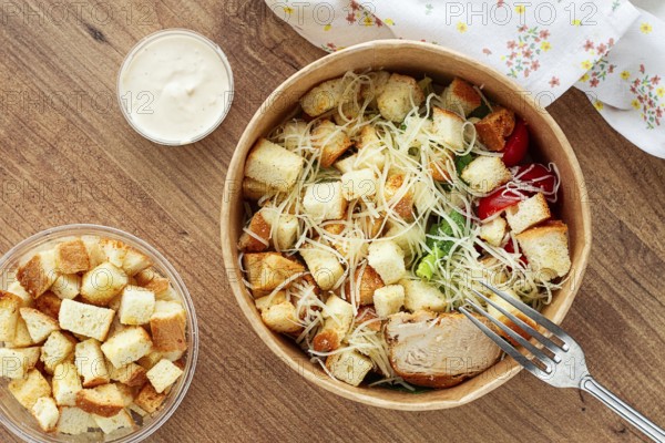 Caesar salad in a paper container, take it on the way, with sauce and croutons, on the table, snack, natural light, no people