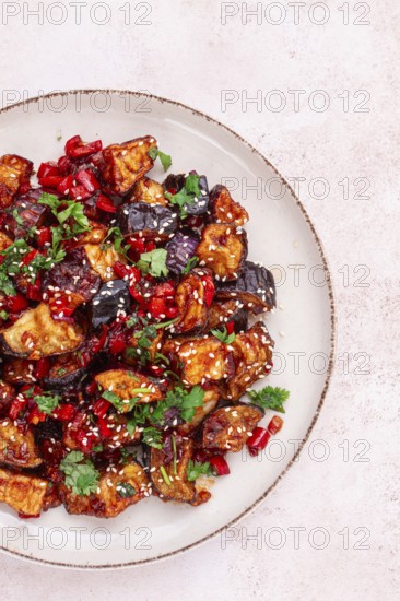 Fried eggplant, Chinese style, in sweet and sour sauce, with pepper and sesame seeds. on a white plate