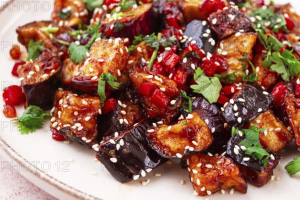 Fried eggplant, Chinese style, in sweet and sour sauce, with pepper and sesame seeds. on a white plate