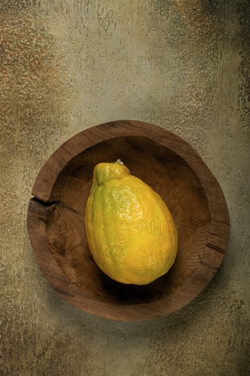 A vibrant yellow papaya is positioned in a rustic wooden bowl, resting on a textured surface that complements its colors, illuminated by gentle, soft light