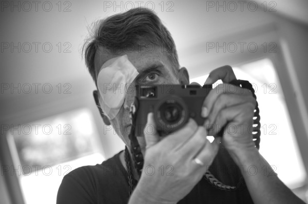 Portrait, self-portrait, selfie, photographer with eye bandage, eye injury, bandage on eye, holding camera, viewfinder camera, photographed, Leica M11 monochrome, black and white, Stuttgart, Baden-Württemberg, Germany