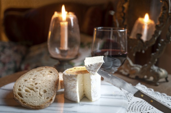 Chaource cheese presented sliced with bread and red wine in warm candlelight, typical of the Champagne region, impresses with its fluffy white mould rind, creamy, mild core and fine, creamy flavours - an artisan cheese with a centuries-old tradition and AOP label, produced by the Fromagerie de Mussy, Chaource, Aube department, Grand Est region, France