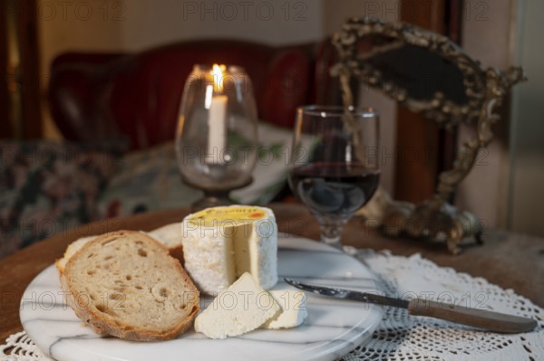 Chaource cheese presented sliced with bread and red wine in warm candlelight, typical of the Champagne region, impresses with its fluffy white mould rind, creamy, mild core and fine, creamy flavours - an artisan cheese with a centuries-old tradition and AOP label, produced by the Fromagerie de Mussy, Chaource, Aube department, Grand Est region, France
