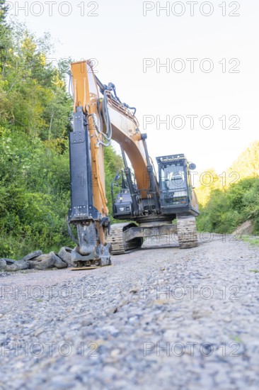 An excavator on a gravel road, surrounded by green bushes, Hermann Hessebahn construction site, Calw, Germany