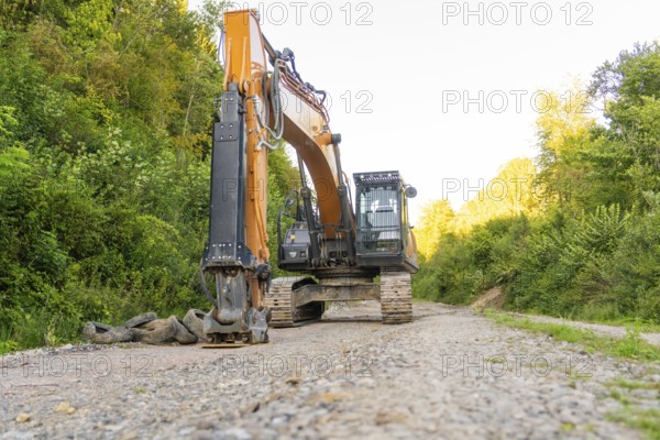 A large excavator stands on a dirt road in a wooded area, Hermann Hessebahn construction site, Calw, Germany