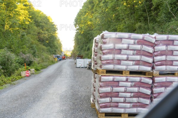 Stacked pallets of building materials line a gravel road in the forest, Hermann Hessebahn construction site, Calw, Germany