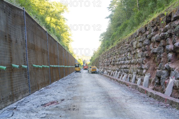 Machines on a construction site between steep walls overhung by trees, Hermann Hessebahn construction site, Calw, Germany