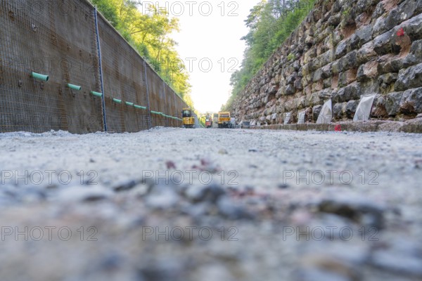 Gravel path between a concrete and a stone wall with construction machinery in the background, Hermann Hessebahn construction site, Calw, Germany