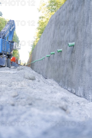 Large concrete wall and blue excavator on a gravel road, Hermann Hessebahn construction site, Calw, Germany