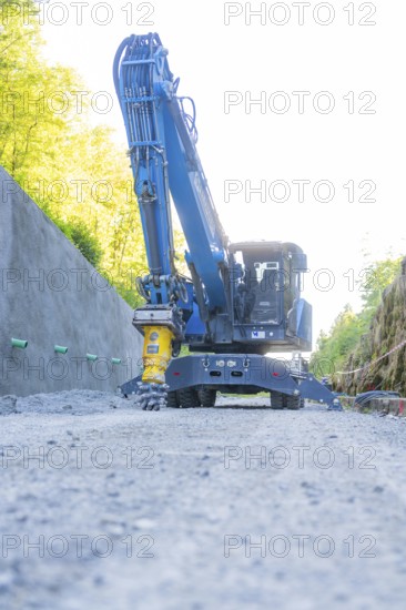Blue excavator with hydraulic hammer on a path on a concrete wall, Hermann Hessebahn construction site, Calw, Germany