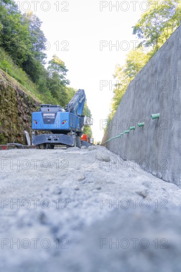 Blue excavator on a path next to a concrete wall with green pipes, Hermann Hessebahn construction site, Calw, Germany