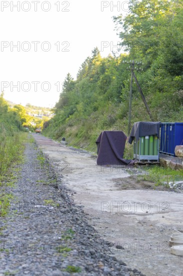 Gravel path with cover and containers along an overgrown embankment, Hermann Hessebahn construction site, Calw, Germany