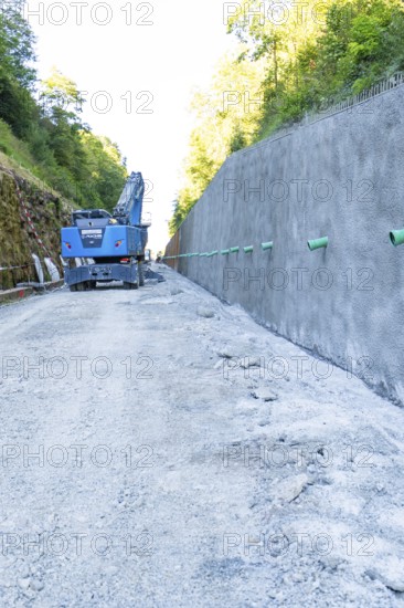 Construction site scene with blue crane next to a high concrete wall and gravel path, Hermann Hessebahn construction site, Calw, Germany
