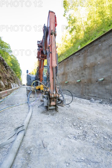 Excavator in action on a construction site next to a concrete wall with pipes, Hermann Hessebahn construction site, Calw, Germany