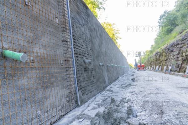 Long concrete wall with reinforcements along a construction site surrounded by trees, Hermann Hessebahn construction site, Calw, Germany