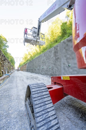 Red lifting platform on a gravel path in front of a concrete wall in the sunshine, Hermann Hessebahn construction site, Calw, Germany