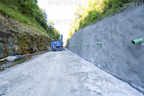 Concrete wall on construction site with blue crane, surrounded by forest and gravel path, Hermann Hessebahn construction site, Calw, Germany