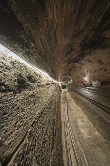 An illuminated tunnel with rails leading into the depths. The walls are made of stone and structured, construction of the Hermann Hesse railway, Calw, Black Forest, Germany