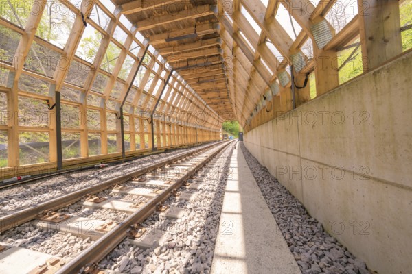 Light-flooded wooden tunnel with railway tracks and concrete path, surrounded by nature, construction of the Hermann Hesse railway, Calw, Black Forest, Germany