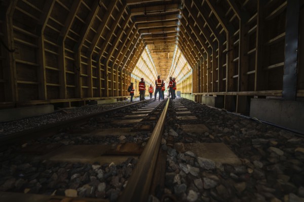 People in safety clothing standing in an illuminated wooden tunnel, construction of the Hermann Hesse railway, Calw, Black Forest, Germany