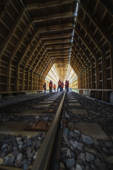 Group of employees in an illuminated wooden tunnel on railway tracks, construction of the Hermann Hesse railway, Calw, Black Forest, Germany