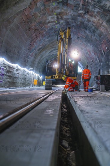 Construction workers in a tunnel carry out work with a large machine. Neon lights illuminate the scene, construction of the Hermann Hesse railway, Calw, Black Forest, Germany