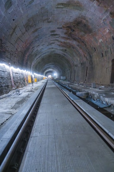 A long, illuminated tunnel with tracks and a deep perspective. The walls appear structured, construction of the Hermann Hesse railway, Calw, Black Forest, Germany