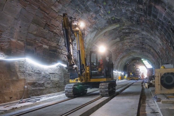 An excavator works on the rails in the illuminated tunnel. The room is structured and bright, construction of the Hermann Hesse railway, Calw, Black Forest, Germany
