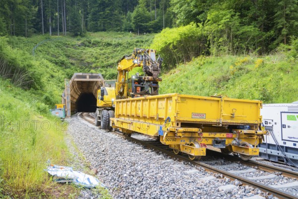 Yellow construction vehicle with equipment near a railway tunnel in green surroundings, construction of the Hermann Hesse railway, Calw, Black Forest, Germany
