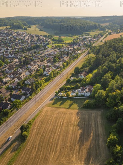 Aerial view of a village with houses, railway tracks and fields, surrounded by forest in the evening light, construction of the Hermann Hesse Railway, Calw, Black Forest, Germany