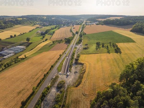 Wide landscape with fields, tracks and a long road, a village visible on the horizon under a blue sky, construction of the Hermann Hesse railway, Calw, Black Forest, Germany