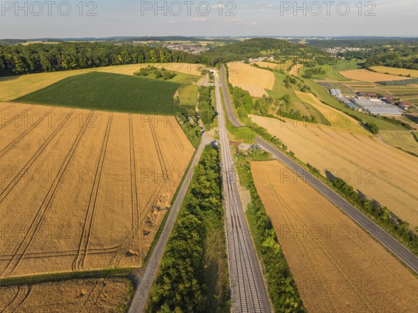 Aerial view of a summer landscape with fields, railway tracks and a road, surrounded by trees and under a blue sky, construction of the Hermann Hesse Railway, Calw, Black Forest, Germany