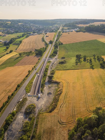Fields and tracks, running parallel to a road, surrounded by trees, with a view of a distant village, construction of the Hermann Hesse railway, Calw, Black Forest, Germany