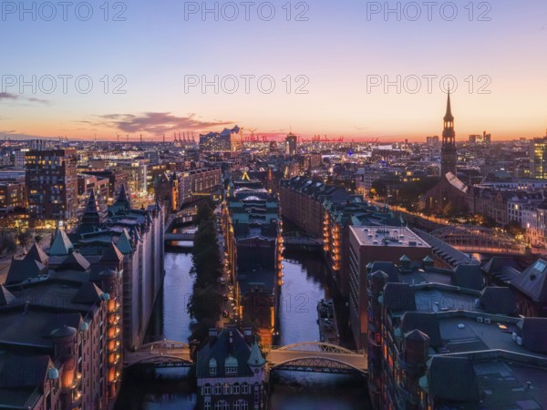 Aerial view of Hamburg's Speicherstadt warehouse district at sunset with a view of the moated castle, the Poggenmühlenbrücke bridge and the Elbphilharmonie concert hall and St Michael's Church in the background, Hamburg, Germany