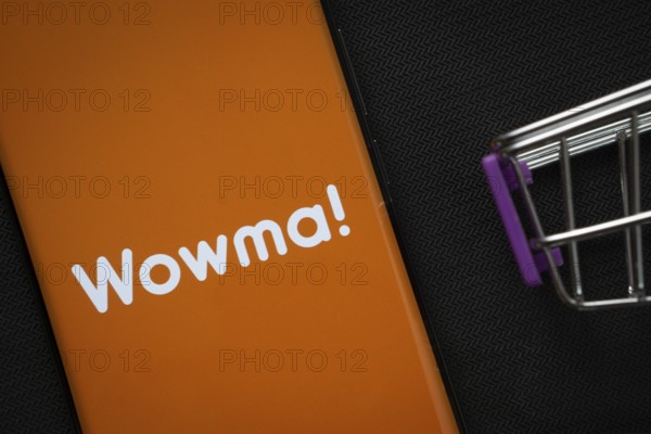 Dhaka, Bangladesh- 03 July 2025: A smartphone displaying the Wowma logo next to a miniature shopping cart on a background