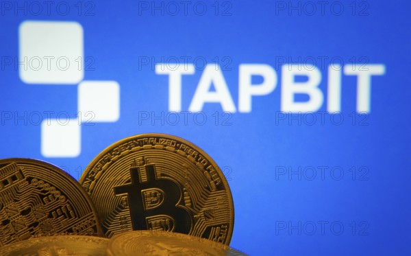 Dhaka, Bangladesh- 20 Sep 2025: Close-up of Bitcoin coins with thex Tapbit logo visible on a screen in the background