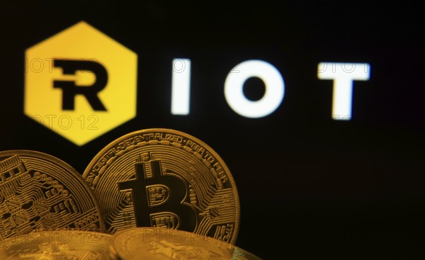 Dhaka, Bangladesh- 20 Sep 2025: Close-up of Bitcoin coins with the Riot Platforms logo visible on a screen in the background