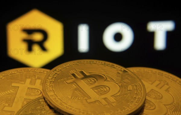 Dhaka, Bangladesh- 20 Sep 2025: Close-up of Bitcoin coins with the Riot Platforms logo visible on a screen in the background
