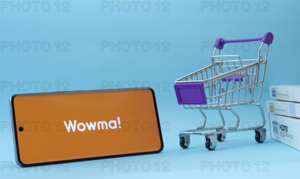 Dhaka, Bangladesh- 03 July 2025: Smartphone with wowma logo next to a small shopping cart and boxes against a blue background